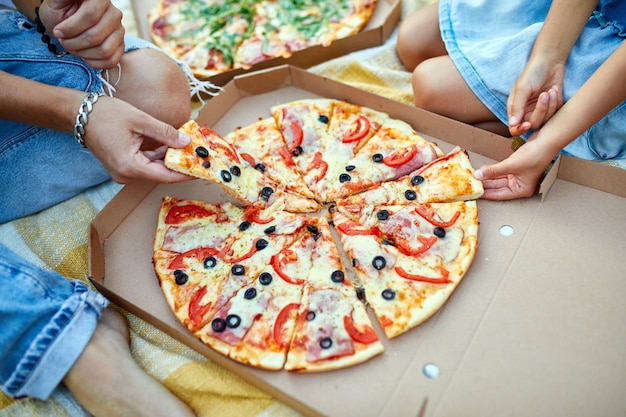 Dzielenie się pizzą, ręce wyciągające kawałek pizzy z pudełka na zewnątrz,
