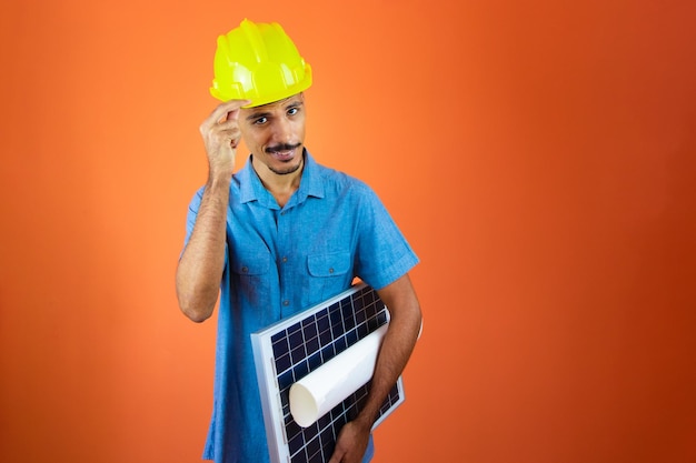 Dzień inżyniera Czarny mężczyzna w kasku ochronnym i niebieskiej koszuli na białym tle Inżynier trzymający fotowoltaiczny panel słoneczny