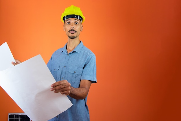 Dzień inżyniera Czarny mężczyzna w kasku ochronnym i niebieskiej koszuli na białym tle Inżynier trzymający fotowoltaiczny panel słoneczny