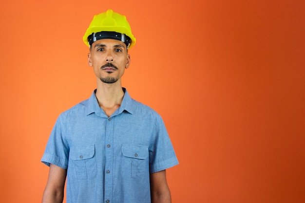 Dzień inżyniera Czarny mężczyzna w kasku ochronnym i niebieskiej koszuli na pomarańczowym tle
