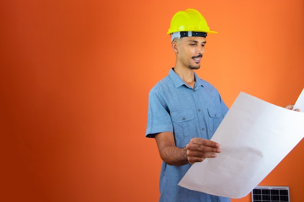 Dzień inżyniera Czarny mężczyzna w kasku ochronnym i niebieskiej koszuli na pomarańczowym tle