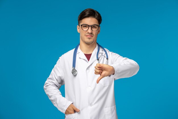 Dzień lekarza ładny młody facet brunetka w fartuchu w okularach pokazujący zły gest
