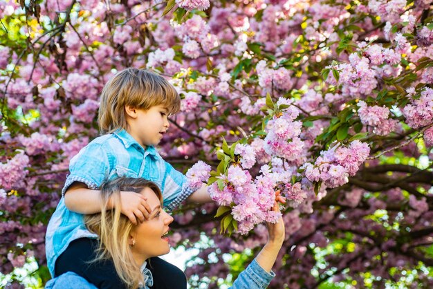 Dzień matki matka i syn szczęśliwa matka jeżdżąca na ramionach w ogrodzie sakura