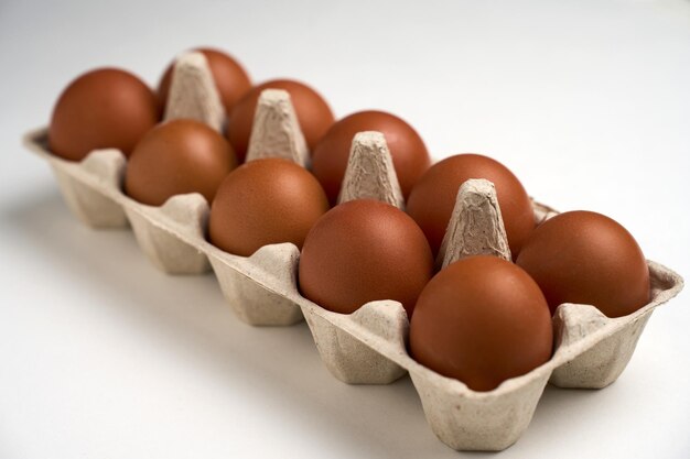 Zdjęcie dziesięć brązowych jaj w kartonie na białym z ścieżką wycinania.