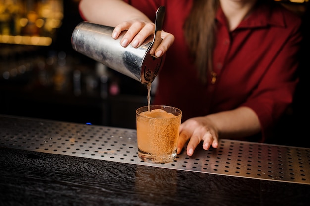 Dziewczyna barman napełniania kieliszka koktajlowego w barze