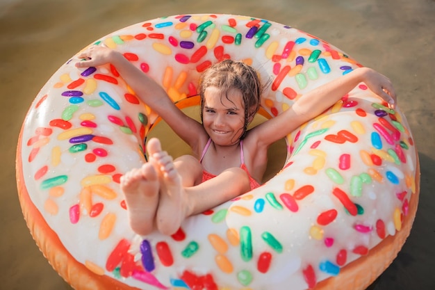Dziewczyna bawi się na dużym nadmuchiwanym pierścieniu z pączkami nad jeziorem w upalny letni dzień szczęśliwej letniej wsi