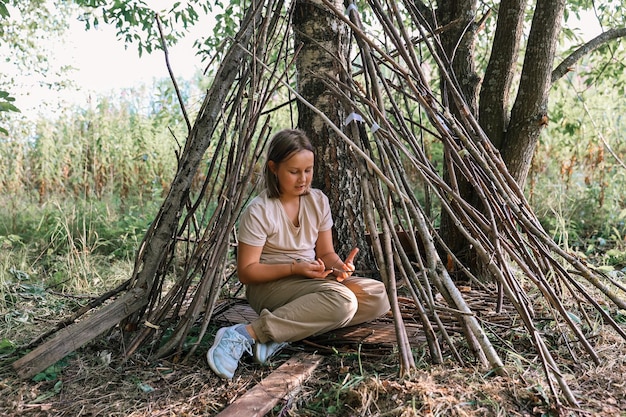 Dziewczyna bawi się w chatce z gałązek i liści. Drewniany dom we wsi