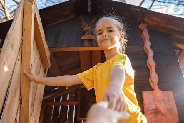 Dziewczyna bawi się w kreatywny, ręcznie robiony domek na drzewie w letniej aktywności na podwórku, szczęśliwe dzieciństwo Cottagecore