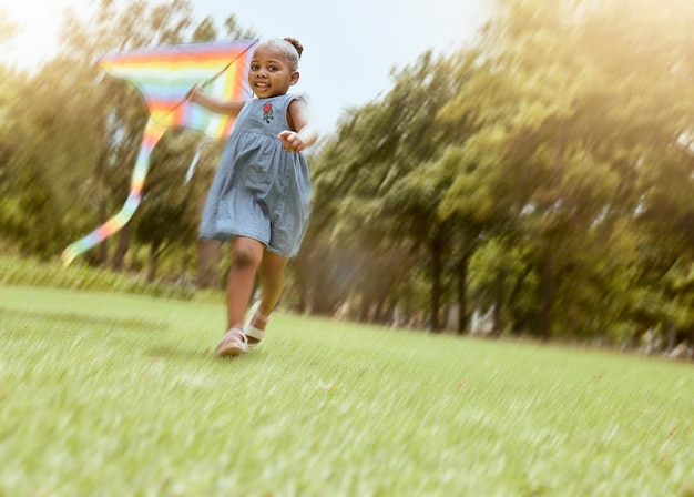 Dziewczyna biegnąca z latawcem i parkiem przyrody dla radosnej zabawy na świeżym powietrzu i wolności biegnącej latem, dzięki czemu pamięć z dzieciństwa Zabawne pole trawy dla dzieci i czarne dziecko bawiące się na zewnątrz podczas wakacji na łonie natury