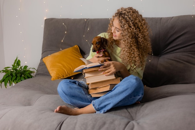 Dziewczyna blondynka z kręconymi włosami ze stosem książek siedzi na łóżku i trzyma psa w ramionach. koncepcja edukacji. czas studencki. styl życia. miejsce na tekst. Zdjęcie wysokiej jakości