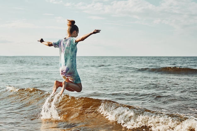 Zdjęcie dziewczyna ciesząca się morzem skacząca przez fale spędzająca wolny czas nad morzem na plaży przy zachodzie słońca