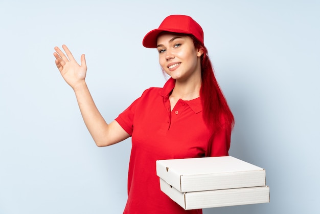 Dziewczyna dostarczająca pizzę trzymająca pizzę nad izolowaną ścianą rozkładającą ręce na bok za zaproszenie