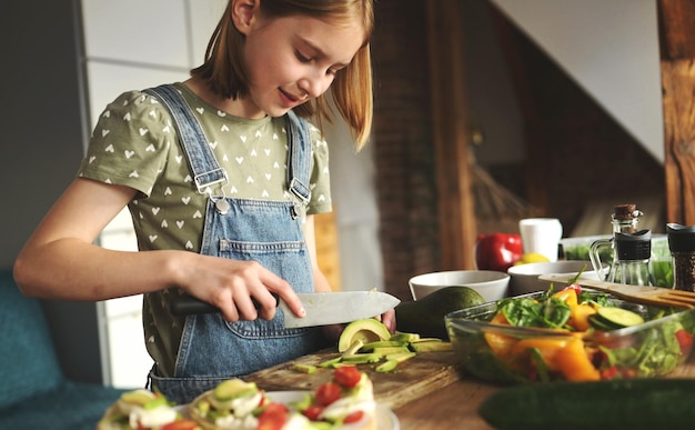 Dziewczyna dziecko tnie avicado nożem w kuchni Pretty samice kid z owoców i warzyw przygotowuje sałatkę