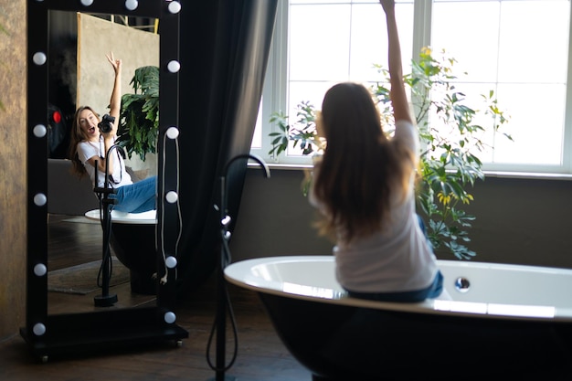 Dziewczyna fotograf z aparatem uśmiecha się siedząc w łazience i patrząc w lustro