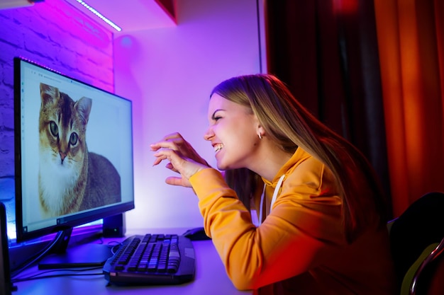 Dziewczyna-freelancerka patrzy na kota na ekranie komputera Siedząc w mieszkaniu przy biurku komputerowym