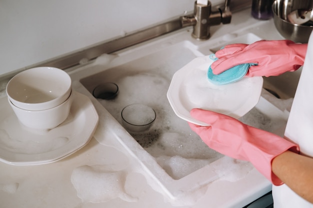 Dziewczyna gospodyni w różowych rękawiczkach ręcznie zmywa naczynia