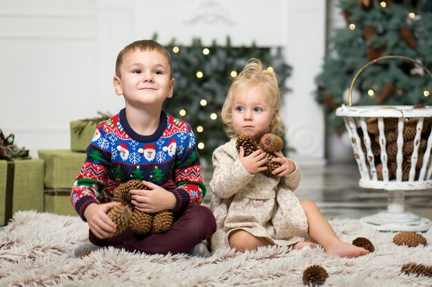 Dziewczyna i chłopak gra na podłodze z szyszek do dekoracji choinki. brat i siostra w pobliżu choinki i pudełka z prezentami. Wesołych Świąt i Wesołych Świąt