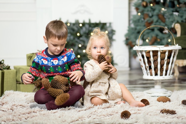 Dziewczyna i chłopak gra na podłodze z szyszek do dekoracji choinki.