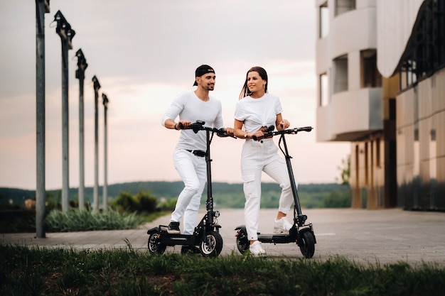 Dziewczyna i chłopak spacerują po mieście na skuterach elektrycznych, zakochana para na skuterach