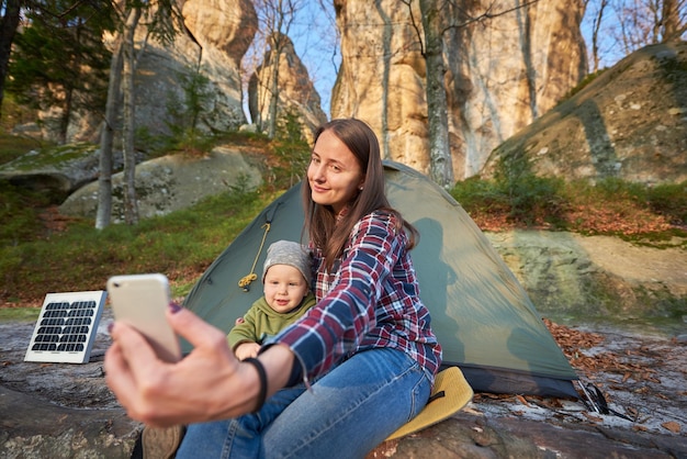 Dziewczyna i dziecko robią sobie selfie na telefonie komórkowym na tle namiotu z baterią słoneczną w lesie