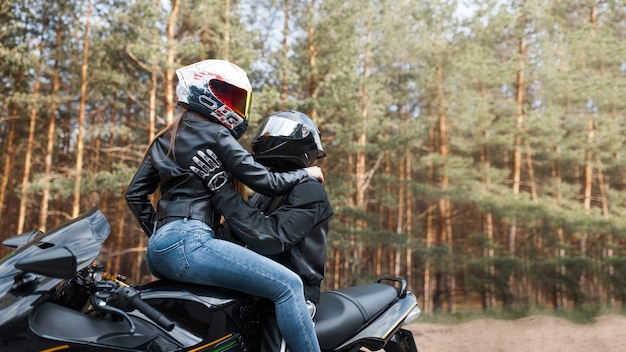 Zdjęcie dziewczyna i facet na sportowym motocyklu w kaskach siedzących razem i przytulających się na rozmytym tle z miejscem na kopię