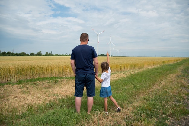 Dziewczyna i jej tata patrzą na generator wiatrowy w polu. Ekologia. Przyszły.