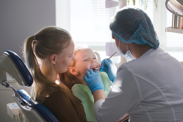 Dziewczyna, jej mama i dentysta w gabinecie stomatologicznym, stomatolog badający i konsultujący, córka bawiąca się i narzekająca, opieka zdrowotna od dzieciństwa