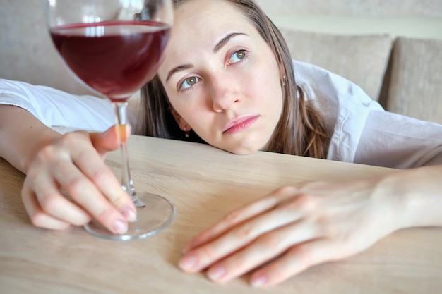 Zdjęcie dziewczyna jest smutna z lampką wina przy stole.