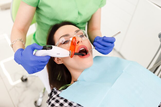 Dziewczyna leczy zęby w stomatologii. Dentysta przy użyciu lampy UV utwardzania zębów na zęby pacjenta