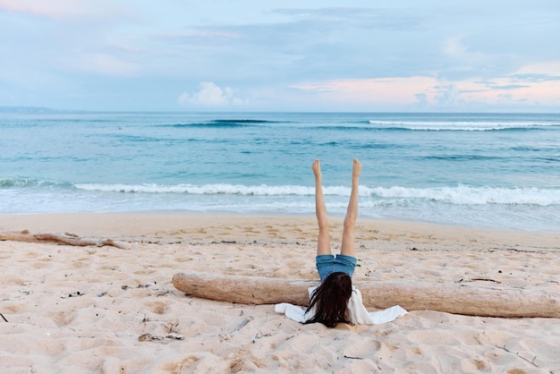 Dziewczyna leżąca na piasku z nogami do góry plecami do kamery na piasku plaży oceanicznej na wyspie na wycieczce relaksacyjnej