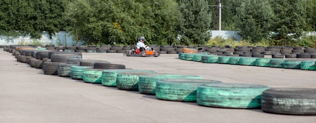 Dziewczyna Lub Kobieta W Kasku Jeździ Gokartem Po Specjalnym Torze Ogrodzonym Gumowymi Kołami. Aktywny Wypoczynek I Sport W Transporcie. Przygotowanie I Treningi Do Zawodów.