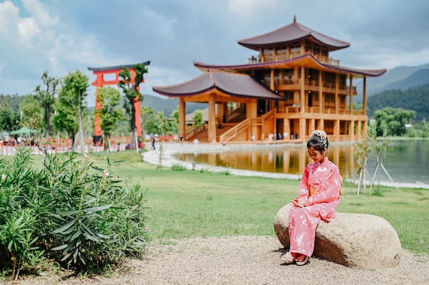 Dziewczyna ma na sobie szczęśliwe kimono Siedzące na kamieniu