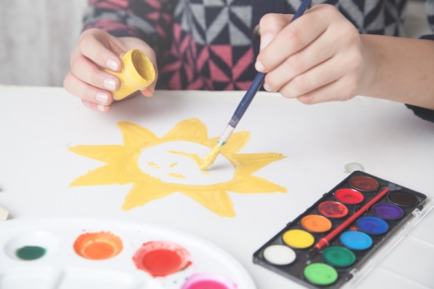 Dziewczyna maluje słońce na papierze pędzlem.