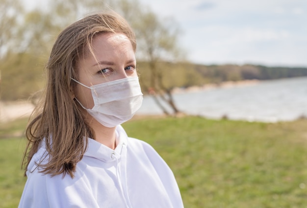 Dziewczyna, młoda kobieta w ochronnej sterylnej masce medycznej na twarzy patrząc na kamery na zewnątrz z bliska.