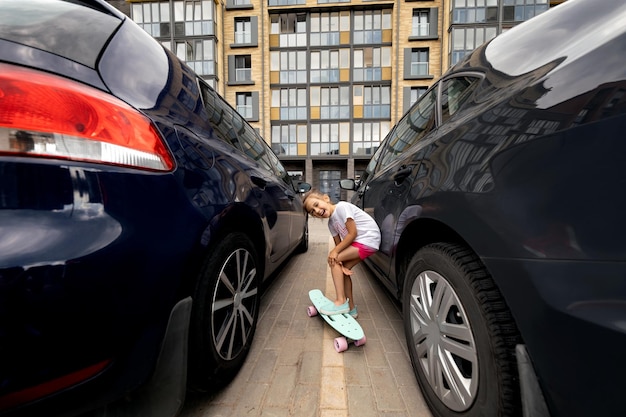 Dziewczyna na deskorolce stoi między dwoma samochodami na parkingu