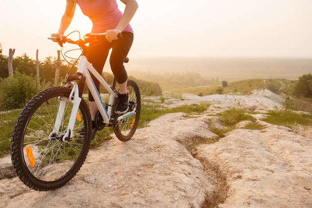 Dziewczyna na rowerze górskim jeździ na szlaku na piękny wschód słońca