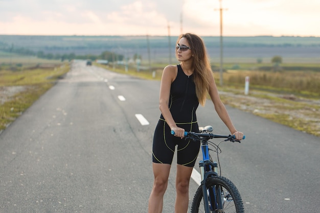 Dziewczyna na rowerze górskim na offroad piękny portret rowerzysty o zachodzie słońca Dziewczynka fitness jeździ na nowoczesnym rowerze górskim z włókna węglowego w odzieży sportowej kask okulary i rękawiczki