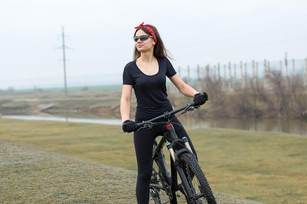 Dziewczyna na rowerze górskim na offroad piękny portret rowerzysty w deszczową pogodę Dziewczynka fitness jeździ na nowoczesnym rowerze górskim z włókna węglowego w odzieży sportowej Portret zbliżenie dziewczyny w czerwonej chustce