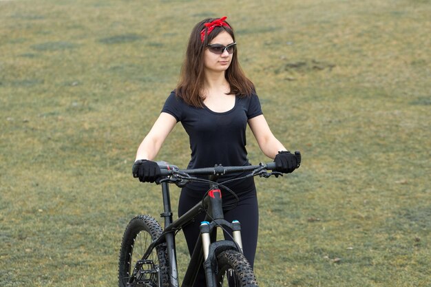 Dziewczyna na rowerze górskim w terenie piękny portret rowerzysty o zachodzie słońca Dziewczynka fitness jeździ na nowoczesnym rowerze górskim z włókna węglowego w stroju sportowym Portret dziewczynki w kasku i okularach