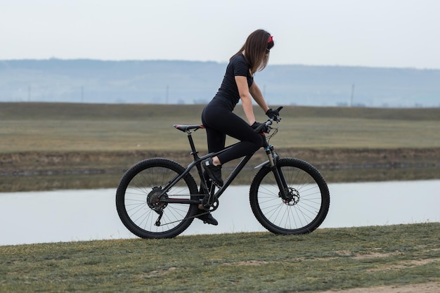 Zdjęcie dziewczyna na rowerze górskim w terenie piękny portret rowerzysty w deszczową pogodę dziewczynka fitness jeździ na nowoczesnym rowerze górskim z włókna węglowego w odzieży sportowej portret zbliżenie dziewczyny w czerwonej chustce