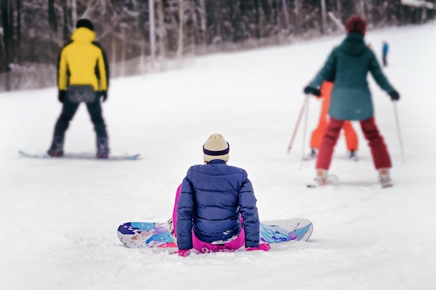 Dziewczyna na snowboardzie w sprzęcie uczy się jeździć z ośnieżonego zbocza góry