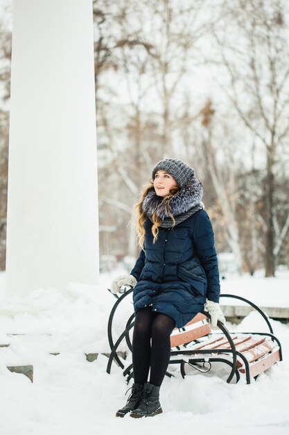 Dziewczyna o europejskim wyglądzie spaceruje po parku, lesie, zimie i śniegu, ubrana w ciepłe ubrania, kapelusz, kurtkę, szalik, odpoczynek, piesze wycieczki