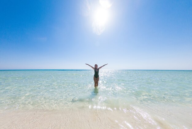 Dziewczyna o pięknej sportowej sylwetce cieszy się ciepłą, błękitną wodą czerwonego morza na piasku