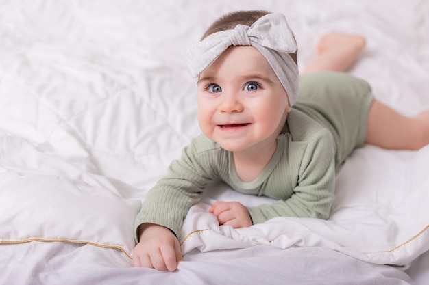 Dziewczyna o pięknych dużych oczach pociera dziecko w domu na łóżku w bawełnianym body na białej pościeli