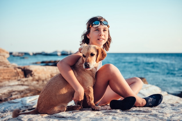 Dziewczyna Obejmuje Jej Psa Podczas Gdy Siedzący Na Skalistej Plaży