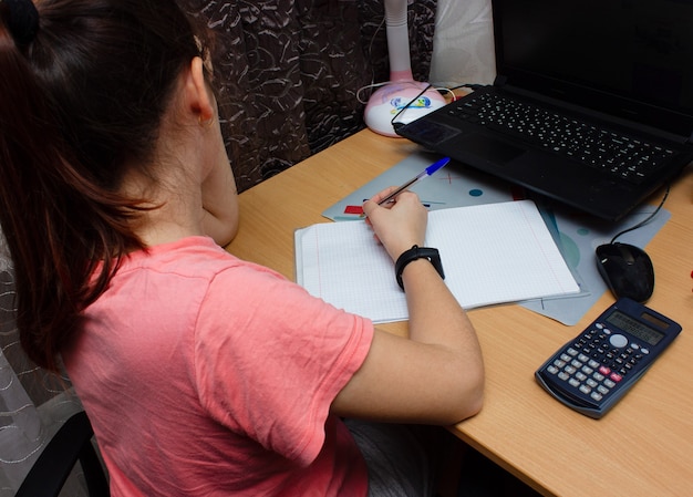 Zdjęcie dziewczyna odrabia pracę domową z matematyki. siedzi przy biurku, pisze piórem w podręczniku. nauka online.