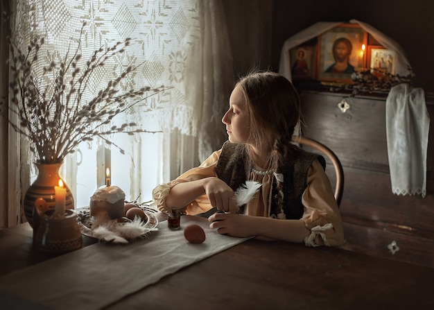 Dziewczyna Odwraca Się Od Malowania Jajek I Wygląda Przez Okno. Portret Młodej Dziewczyny Przy Stole. Przygotowania Do Wielkanocy W Rosyjskiej Wiosce.