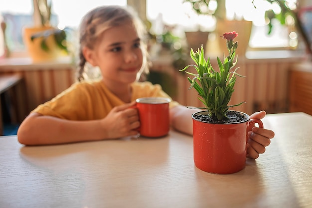 Dziewczyna pijąca kawę i ciesząca się zielonym kwitnącym kwiatem przesadzonym w czerwonym kubku kwiatowy wystrój domu