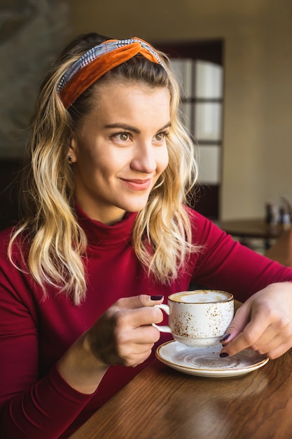 Dziewczyna pije cappuccino w kawiarni, siedząc przy stoliku przy oknie.