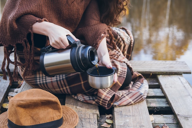 Dziewczyna pije herbaty na drewnianym moscie na jeziorze